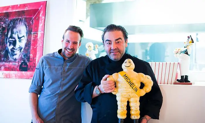 22 Guide Michelins stehen mit dem Buchrücken zur Küche: Juan Amador und Küchenchef Sören Herzig mit einem rund 90 Jahre alten Guide-Michelin-Männchen