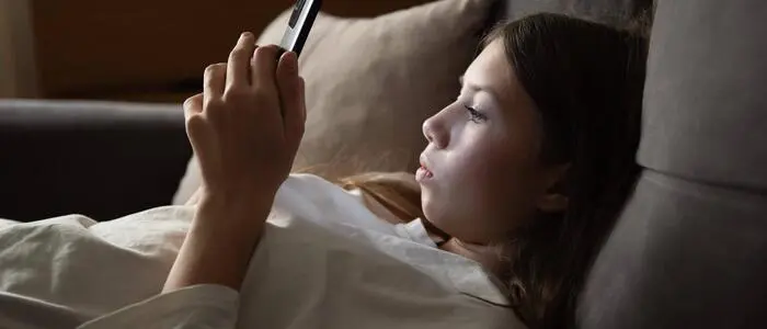 Ein Mädchen liegt auf einem Sofa und blickt in ihr Smartphone.