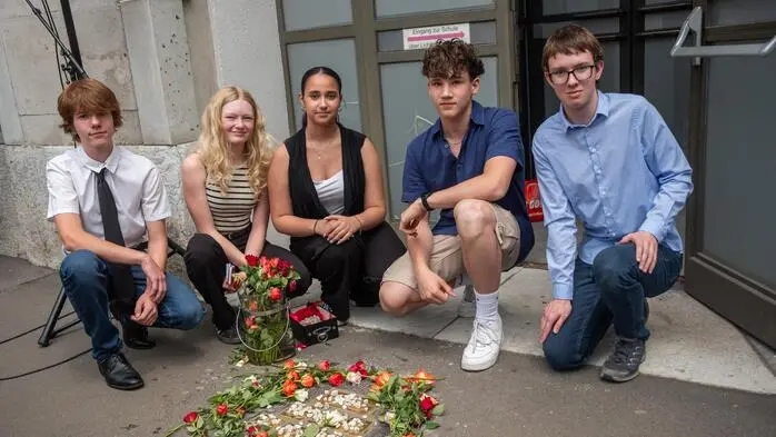 Gruppenfoto der Schüler, vorne sind die Gedenktafeln im Asphalt mit Blumen und Steinen geschmückt | Alexander Mohr, Greta Bugram, Valentina Ajdanov, Tamino Tschernatsch und Markus Schreiber vor den Stolpersteinen beim Lichtenfels-Gymnasium