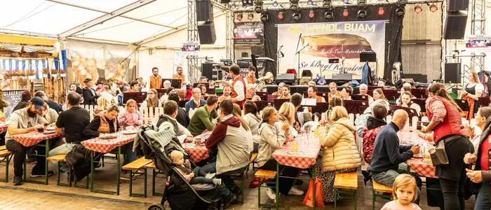 Viele Menschen sitzen vor einer Bühne an Tischen in einem Zelt | Zum Essen und Feiern gehört für viele die Musik