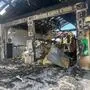 Man sieht ein ausgebranntes Gebäude und zwei ausgebrannte Fahrzeuge darin