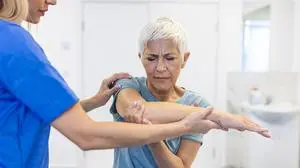 Happy senior woman doing exercise with physiotherapist. Old retired lady doing stretching arms at clinic with the help of a personal trainer during a rehabilitation session.