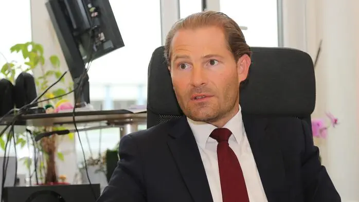Ein Mann im Anzug sitzt an einem Schreibtisch und spricht