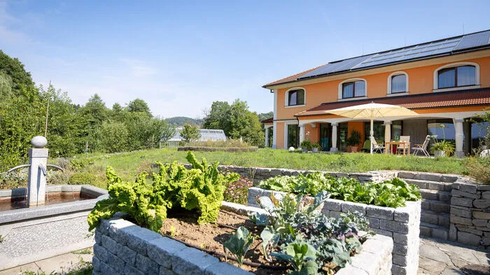 Der Blick vom Areal mit den steinernen Hochbeeten über die Wiese zum Haus