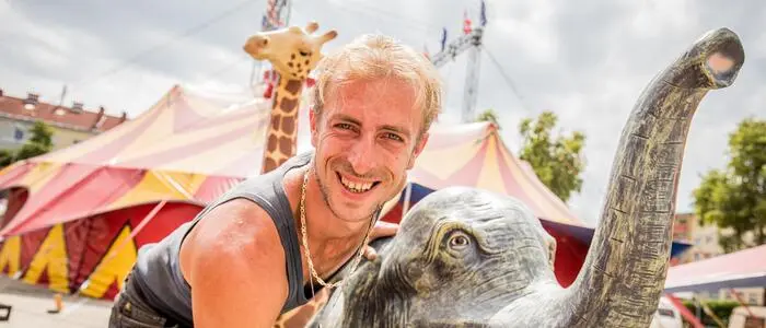 Ein Mann mit einem steinernen Elefanten lächelt in die Kamera.