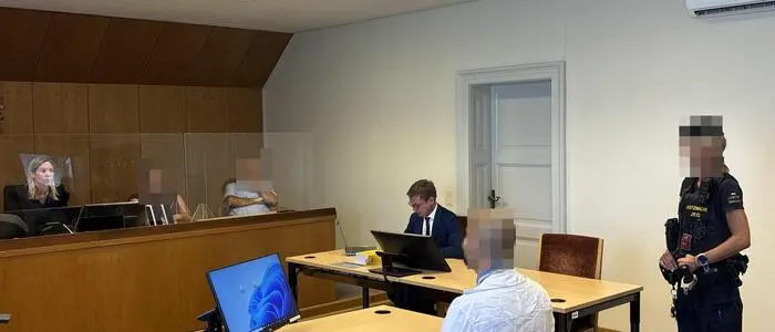 Man sieht den Angeklagten, daneben eine Justizwachebeamte, daneben den Verteidiger und gegenüber die Richterin und die zwei Schöffen