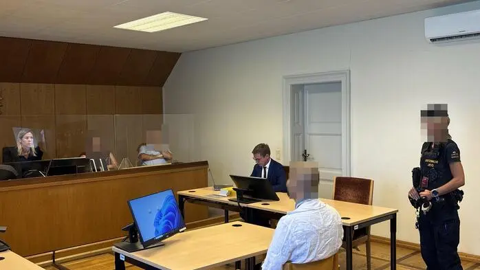 Man sieht den Angeklagten, daneben eine Justizwachebeamte, daneben den Verteidiger und gegenüber die Richterin und die zwei Schöffen