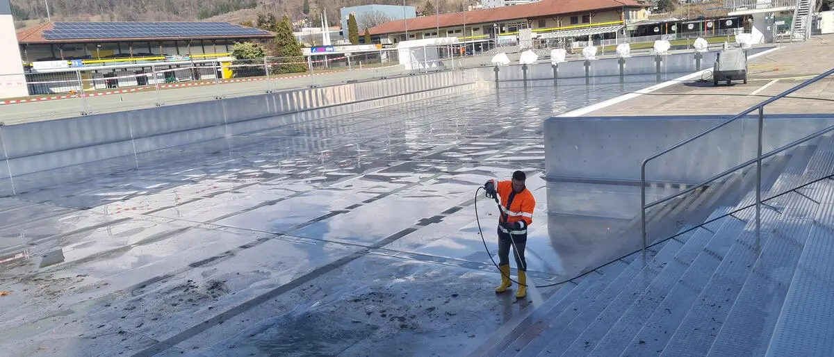 Ein Mann reinigt mit einem Hochdruckreiniger ein Edelstahlbecken in einem Freibad