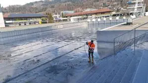 Ein Mann reinigt mit einem Hochdruckreiniger ein Edelstahlbecken in einem Freibad