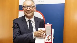 Ein Mann im dunklen Anzug und Brille hält eine Urkunde und eine Medaille in die Kamera