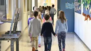 Mehrere Volksschulkinder gehen in Zweierreihen durch einen Schulgang