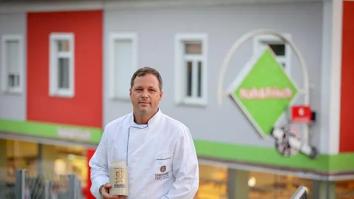Ein Mann in einer Kochuniform hält einen tönernen Bierkrug in seinen Händen