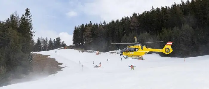 Eine Skipiste, auf der ein gelber Hubschrauber zu landen versucht.