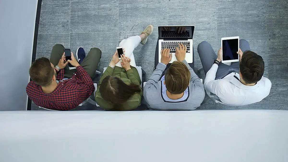 Group of attractive young people sitting on the floor using a laptop, Tablet PC, smart phones, smiling