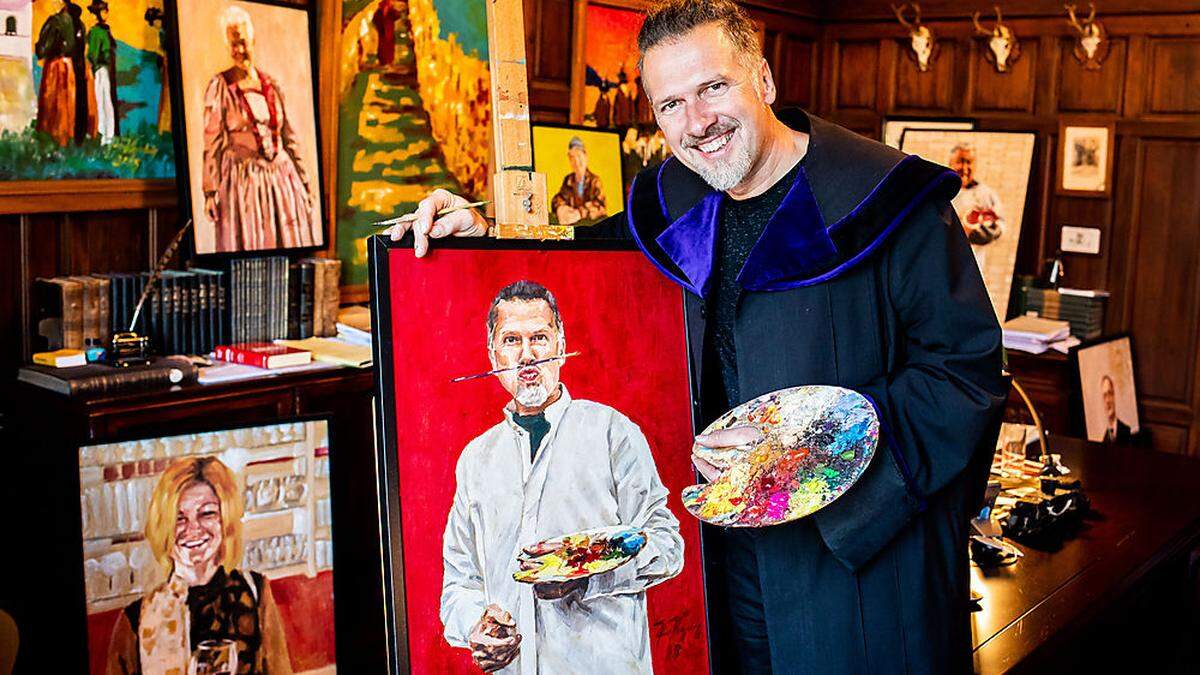 Johann Kogelnig in seinem Büro mit einem Selbstporträt und einigen der Bilder, die in der Ausstellung zu sehen werden sein