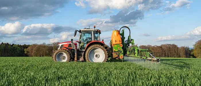 Ein Traktor versprüht Pflanzenschutzmittel auf einem grünen Feld