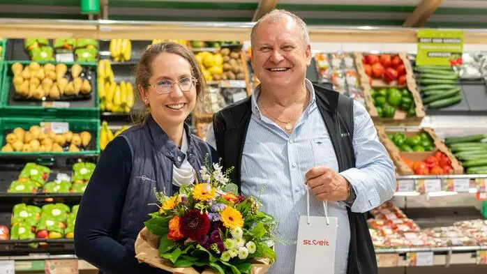 Zwei Menschen stehen in einem Lebensmittelgeschäft und lächeln in die Kamera