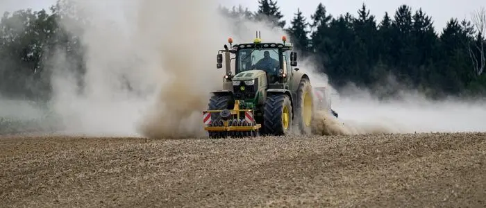 Ein Traktor mit landwirtschaftlichen Anbaugeräten und Sämaschine bearbeitet einen trockenen Acker
