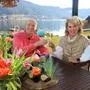 Ein älterer Herr und eine Dame sitzen an einem Tisch, im Hintergrund ist ein See, der Tag ist sonnig