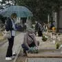 People adjust flowers on the tomb of a relative at the Monumental Cemetery of Bergamo, Lombardy, a day after it reopened on May 19, 2020 as the country's is easing its lockdown aimed at curbing the spread of the COVID-19 infection, caused by the novel coronavirus. - A new area in the cemetery of Bergamo is being dedicated to some of the people who have died in recent weeks and who have expressly asked to be buried in the ground and not cremated, and who do not have a family tomb or burial place. (Photo by Piero CRUCIATTI / AFP)