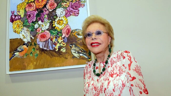 Heidi Goess-Horten neben dem Bild, das sie selbst gemalt hat. Es zeigt einen Blumenstrauß mit drei Vögeln.