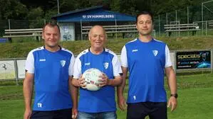 Drei Herren posieren für ein Foto. Einer hält einen Fußball in den Händen.