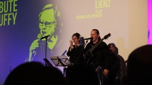 Ein Musiker und eine Musikerin auf der Bühne in Lienz. Im Hintergrund ist ein Bild des verstorbenen Künstlers Buffy zu sehen |  17 Musikerinnen und Musiker performten in unterschiedlichsten Besetzungen zahlreiche Songs zu Ehren von „Buffy“