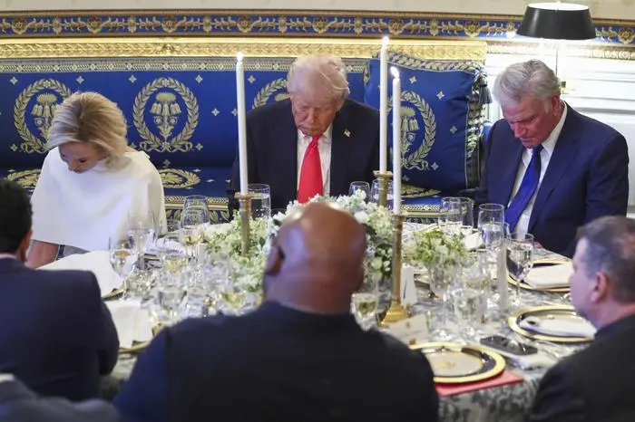 President Donald Trump bows his head during a prayer at an Easter prayer service and dinner in the Blue Room of the White House in Washington, Wednesday, April 16, 2025, with Pastor Paula White, left, and Rev. Franklin Graham, right. (Pool via AP)