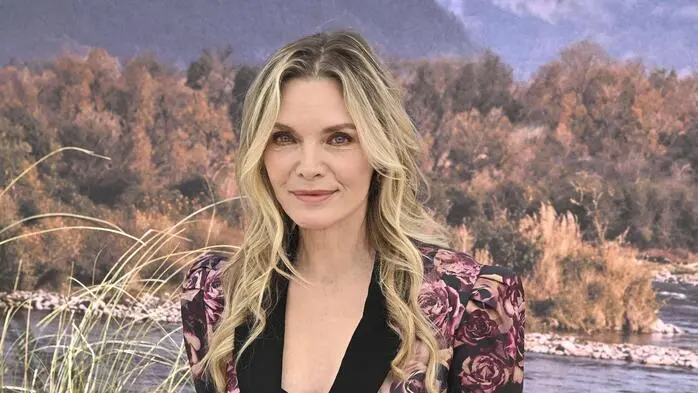 Michelle Pfeiffer in einem Kleid mit Blumenmuster vor einer Leinwand mit einer Wasserlandschaft.