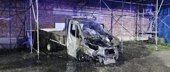 Ein verbrannter Klein-Lkw steht unter einem Gerüst nahe einer Hausmauer
