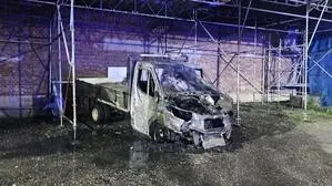 Ein verbrannter Klein-Lkw steht unter einem Gerüst nahe einer Hausmauer