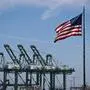 The US flag blows in the wind as trucks drive on the Vincent Thomas Bridge past cranes to unload cargo shipping containers at the Port of Los Angeles in San Pedro, California on April 10, 2025. US President Donald Trump's 10 percent tariff for almost all countries except China will likely remain in place going forward, his top economic advisor Kevin Hassett said Thursday. On April 8, Trump announced a 90-day pause on higher tariffs against all countries except China, reversing a policy that had roiled global stock markets and spooked the American bond markets -- a key barometer of investors' faith in the US government's ability to pay its debts. (Photo by Patrick T. Fallon / AFP)