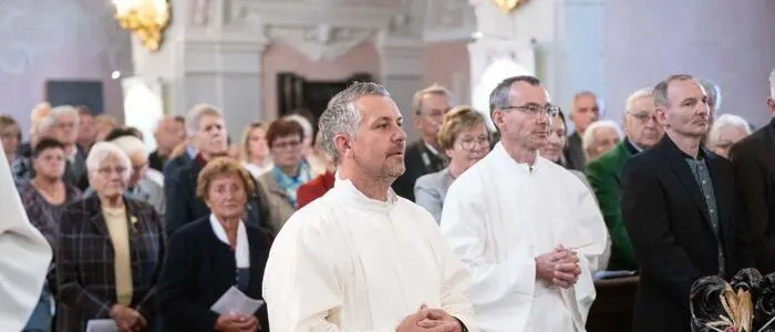 Zwei Männer in Priesterkleidung in einer vollen Kirche