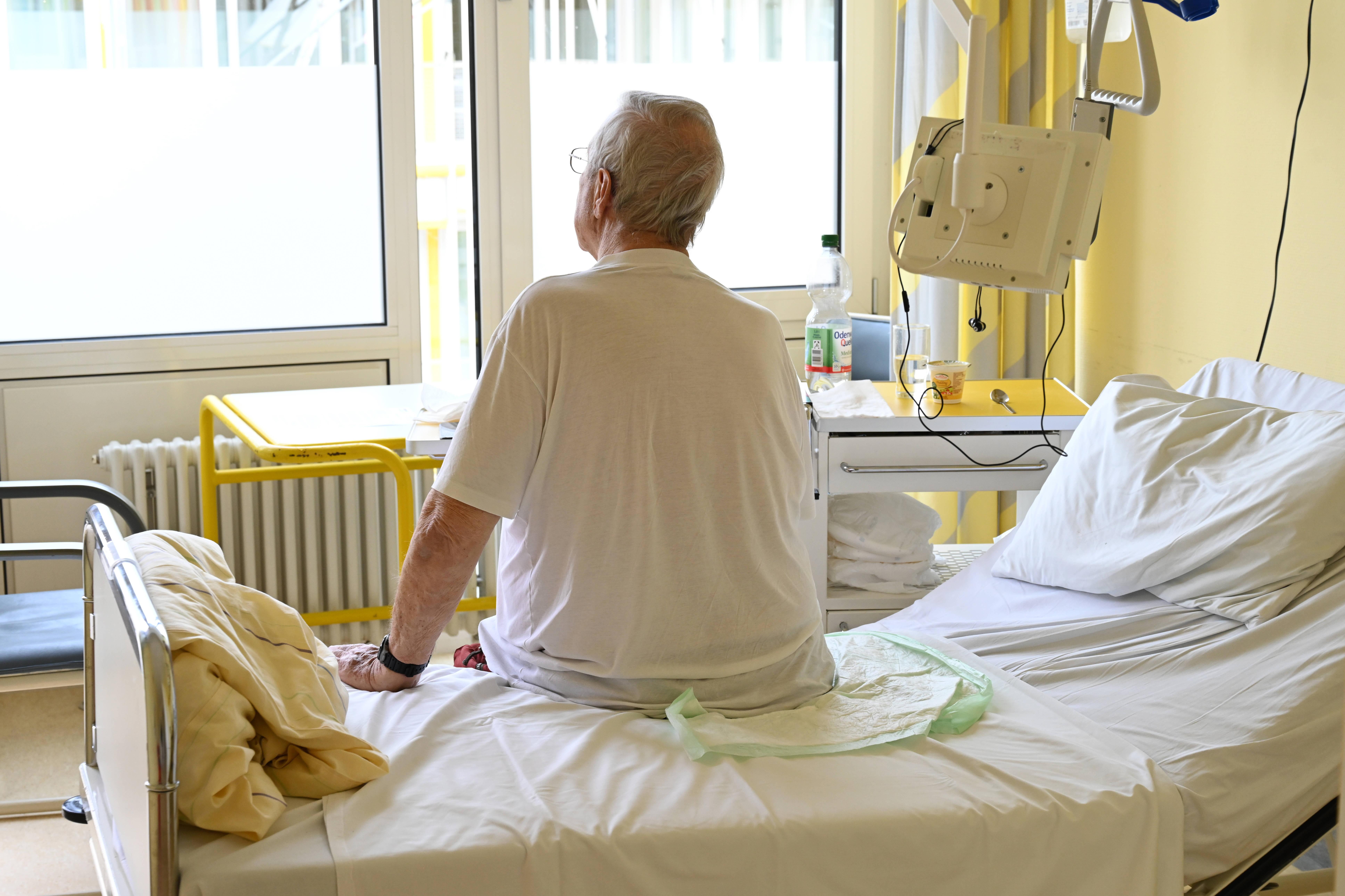 Ein Patient sitzt auf einem Spitalsbett und schaut aus dem Fenster
