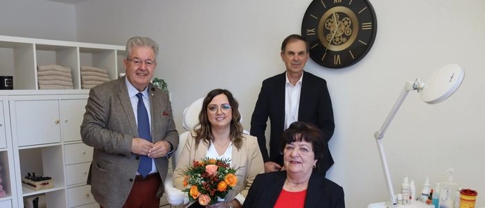 Zwei Männer und zwei Frauen befinden sich in einem Fußpflegestudio, eine Frau hält einen Blumenstrauß in der Hand.