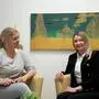 Zwei blonde Frauen sitzen auf zwei gelben Stühlen, beide lachen