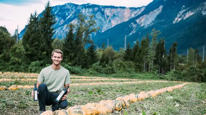 Ein junger Mann kniet in einem Feld mit Kürbissen und hält Flaschen in der Hand