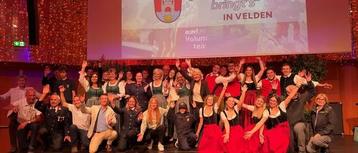 Eine Gruppe von Menschen steht auf einer Bühne, winkt und lächelt