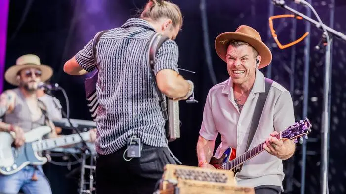 Ein Sänger steht mit Gitarre auf einer Bühne.