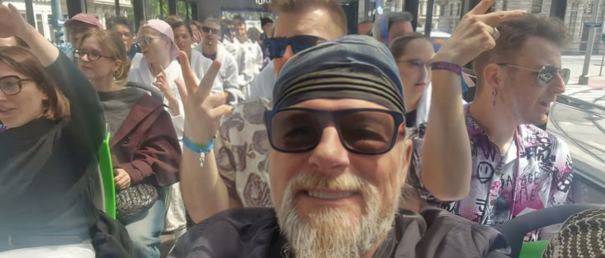 Ein bärtiger Mann mit Sonnenbrille lacht in die Kamera - dahinter sind viele Menschen