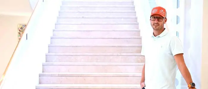 Ein Mann, Johannes Kirisits, steht an der Treppe und lehnt sich an das rechte Geländer. | Johannes „Joe“ Kirisits erzählt über sein bewegtes Leben