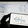 Person holding cellphone with logo of European fund rating company Scope Group on screen. Stuttgart, Germany - 03-13-2023: Person holding cellphone with logo of European fund rating company Scope Group on screen in front of business webpage. Focus on phone display. Copyright: xZoonar.com/TimonxSchneiderx 20015015