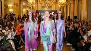 Mehrere Frauen in bunten Kleidern auf einem Laufsteg, daneben Zuschauer