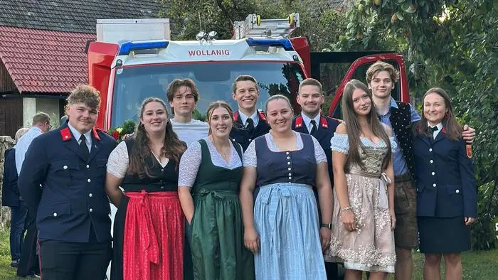 Junge Männer und Frauen in Tracht und Feuerwehruniform stehen vor einem Feuerwehrauto