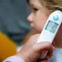 Mother takes temperature for her little preschool daughter, sick child with infrared in ear thermometer at home, high grade fever Mother hand holding digital infrared thermometer