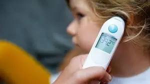 Mother takes temperature for her little preschool daughter, sick child with infrared in ear thermometer at home, high grade fever Mother hand holding digital infrared thermometer