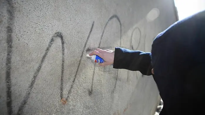 Ein vermummter Täter sprüht Graffiti auf eine Wand.