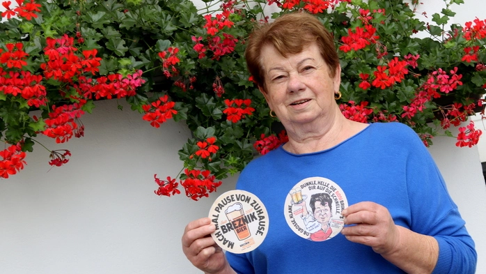 Eine Dame im blauen Leiberl hält zwei Bierdeckel hoch 
