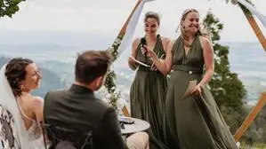 Ein Brautpaar sitzt auf Stühlen, zwei Frauen stehen vor ihnen mit einem Mikrofon, der Ausblick zeigt das Lavanttal und Berge