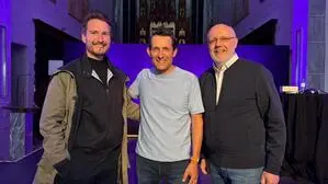 Drei Männer lachen in die Kamera, sie stehen in einer Domkirche